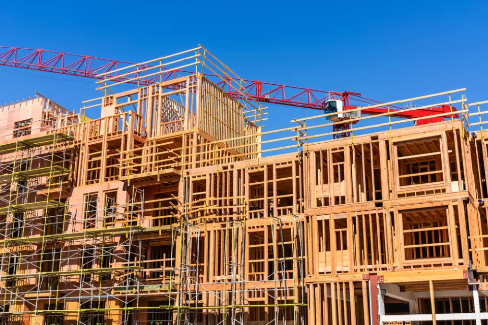 Wood-framed apartment building under construction with red crane in background